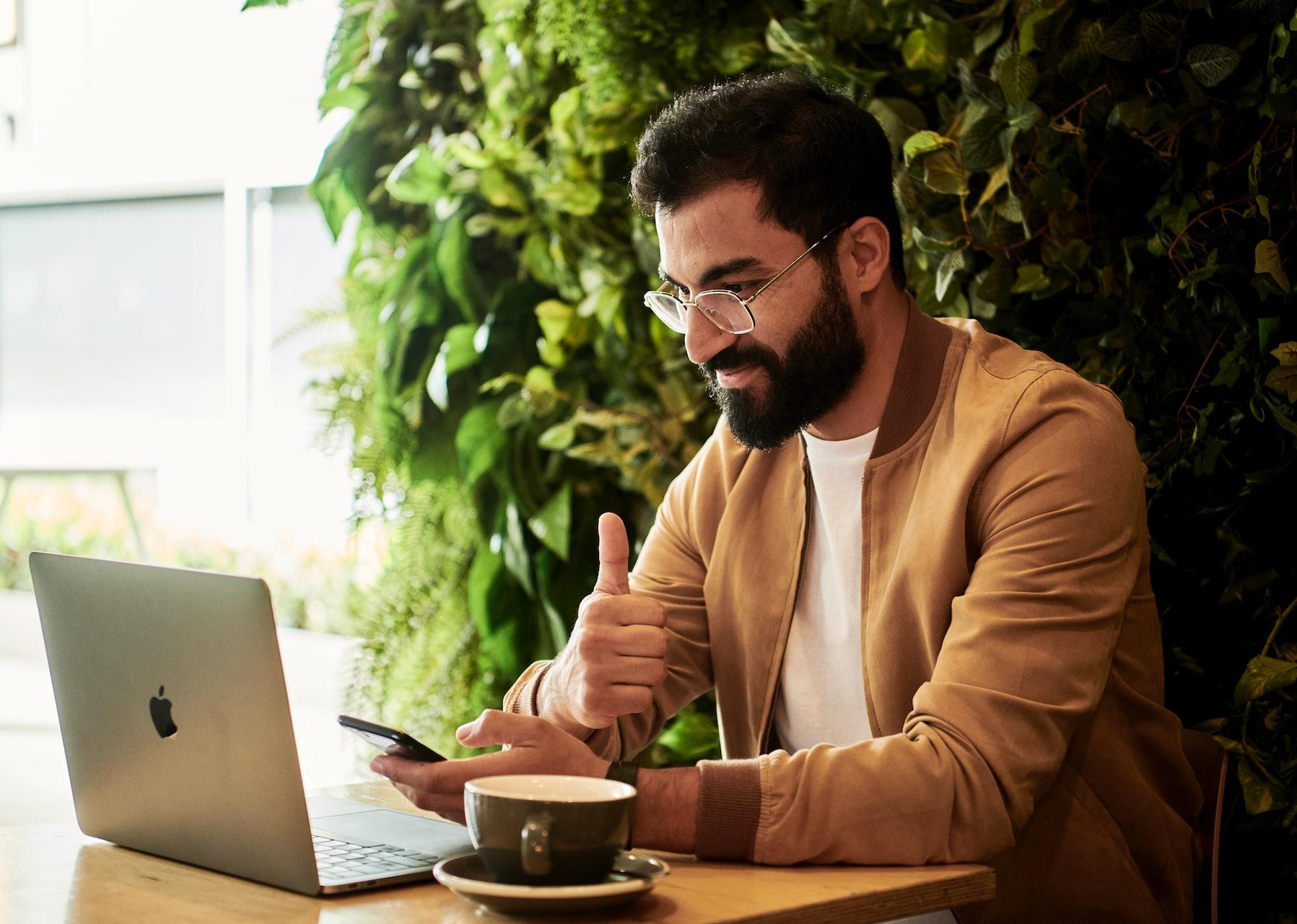 man in brown jacket sitting at a table looking at laptop